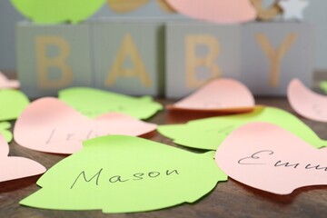 Paper stickers with different names on wooden table, closeup. Choosing baby's name