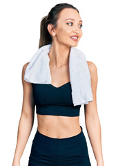 Beautiful caucasian woman wearing sportswear and towel looking away to side with smile on face, natural expression. laughing confident.