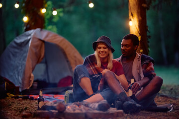 Young couple relaxing by campfire in nature in evening.