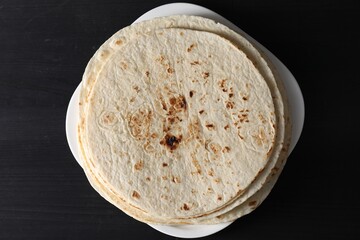 Many tasty homemade tortillas on black wooden table, top view