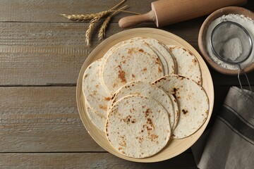 Many tasty homemade tortillas and rolling pin on wooden table, top view