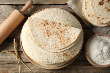 Tasty homemade tortillas, flour, rolling pin and spikes on wooden table, flat lay