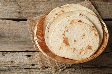 Tasty homemade tortillas in wicker basket on wooden table, space for text