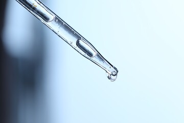 Dripping liquid from pipette on light blue background, closeup