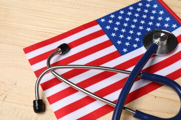 Stethoscope and USA flag on wooden table, closeup. Health care concept