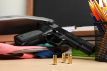 Gun, bullets and school stationery on wooden table, closeup