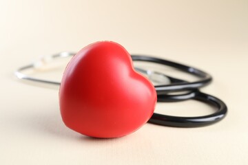 Stethoscope and red heart on beige background, closeup