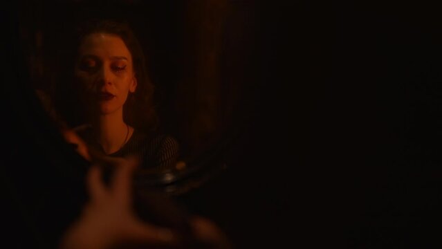 Mysterious reflection on mirror of enigmatic fortune teller on black robe shuffling Tarot cards forecasting future in dark room. Mystery wizard having divination session with tarot cards indoors.