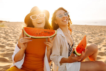 Female friends on vacation at the beach in summer eating a watermelon with the sea in the...