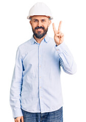 Young handsome man wearing architect hardhat showing and pointing up with fingers number two while smiling confident and happy.