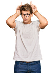 Fototapeta premium Handsome caucasian man wearing casual clothes and glasses doing funny gesture with finger over head as bull horns