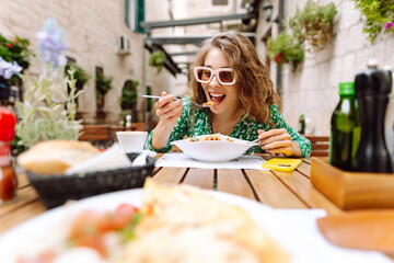 Young woman sitting in summer cafe, eating pasta with tomato, meat. Bolognese. Parmesan cheese....