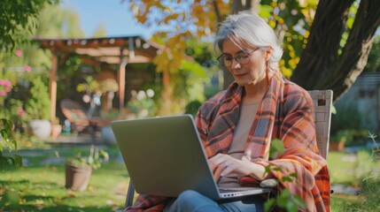 Obraz premium Modern handsome middle-aged woman in nice comfortable clothes working with laptop in home garden