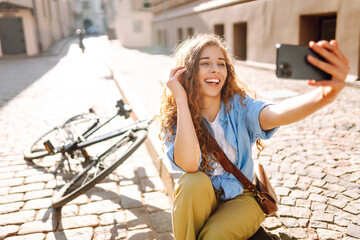 Young woman with bike outdoors in park in summer day using mobile phone. Selfie time. Travel,...