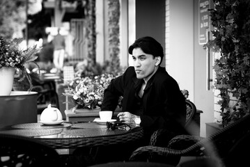 Handsome asian man in suit sits in cafe, drinks tea. bw. Grainy photo