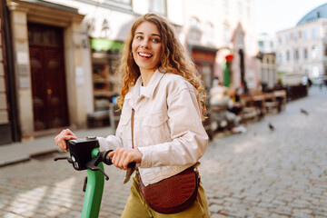 Beautiful woman rides an electric scooter in the city street on a sunny day. Ecological transport....