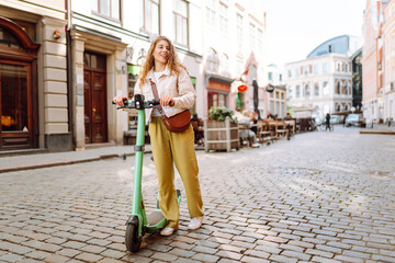 Beautiful woman rides an electric scooter in the city street on a sunny day. Ecological transport....