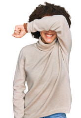 Young hispanic girl wearing wool winter sweater covering eyes with arm smiling cheerful and funny. blind concept.