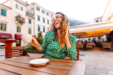 Woman in outdoors street coffee shop cafe sitting at table with cup of coffee, relaxing in...