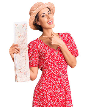 Young beautiful woman wearing summer hat holding map smiling happy pointing with hand and finger