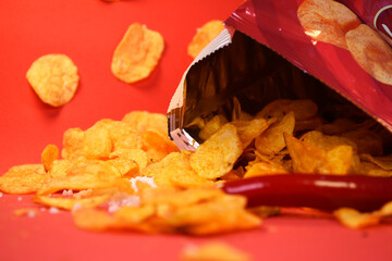 Spicy chips with pepper and salt on a red background scattered on the surface from the packaging