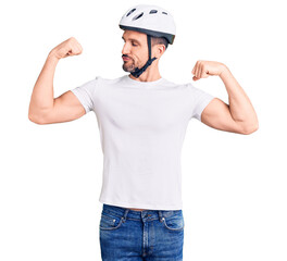 Young handsome man wearing bike helmet showing arms muscles smiling proud. fitness concept.