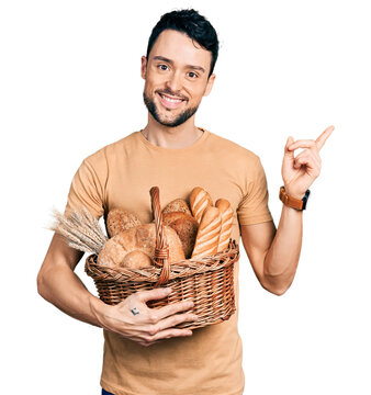 Hispanic man with beard holding wicker basket with bread smiling happy pointing with hand and finger to the side