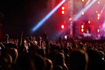 Energetic audience enjoys night music fest, illuminated stage with performers. Fans raise hands,...