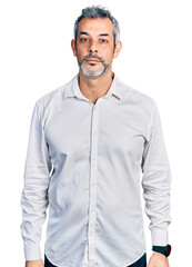 Middle age hispanic with grey hair wearing casual white shirt relaxed with serious expression on face. simple and natural looking at the camera.