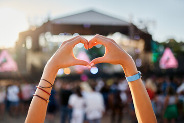 Hands shape heart sign at sunset beach music fest, crowd enjoys live concert. Outdoor summer event,...