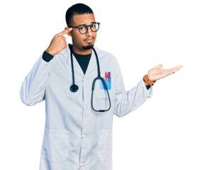 Young african american man wearing doctor uniform and stethoscope confused and annoyed with open palm showing copy space and pointing finger to forehead. think about it.