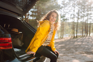 Young woman enjoying nature sitting in open trunk. Journey by car. Lifestyle, travel, tourism, nature concept.