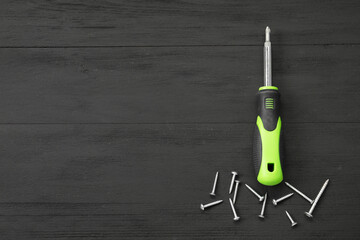Screwdriver with green handle and screws on black wooden table, flat lay. Space for text