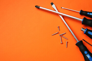 Set of screwdrivers and screws on orange background, flat lay. Space for text