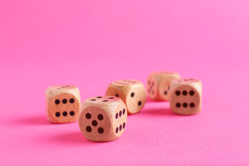 Many wooden game dices on pink background, closeup
