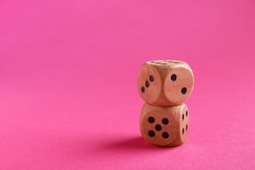 Two stacked wooden game dices on pink background, closeup. Space for text