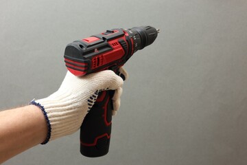 Naklejka premium Handyman holding electric screwdriver on grey background, closeup. Space for text