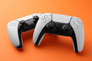 Two wireless game controllers on orange background
