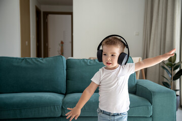 Obraz premium Cute little boy listening to music on headphones, in the living room
