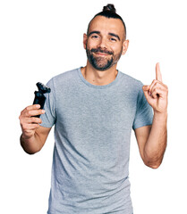 Hispanic man with ponytail holding electric razor machine smiling with an idea or question pointing...