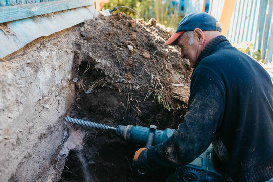 male worker drills the foundation with a hammer drill for sewerage in a country house.