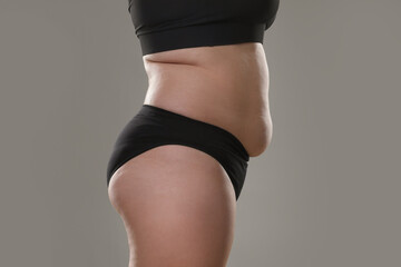 Woman with excessive belly fat on grey background, closeup. Overweight problem