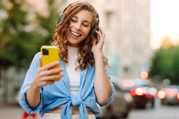 Young woman dancing and listening music with headphones and smart phone in the street. Street...