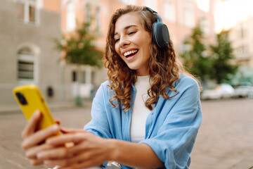 Young woman dancing and listening music with headphones and smart phone in the street. Street...