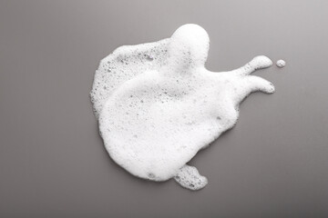 White foam with bubbles on grey background, top view