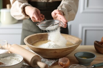 Making dough. Woman sifting flour into bowl at wooden table in kitchen, closeup