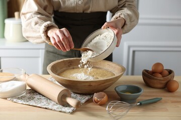 Making dough. Woman adding flour into bowl at wooden table in kitchen, closeup
