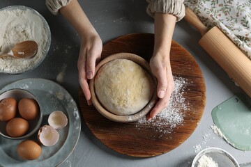 Woman making dough at grey table, top view