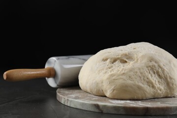 Raw dough and rolling pin on black table, closeup