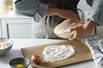 Woman kneading dough at white wooden table in kitchen, closeup